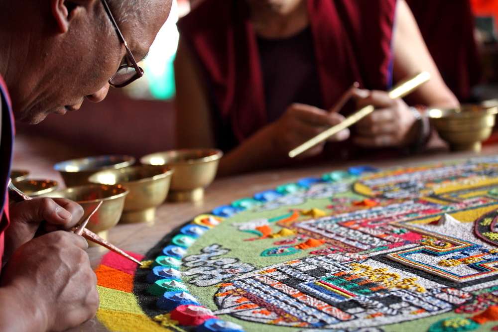 Mehrere Mönche arbeiten an einem Mandala. Quelle: Vladimir Melnik / Shutterstock.com