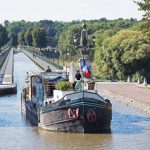 “Fluss des Lebens – Geliebte Loire”: Pierre (Mathieu Delarive) und Romy (Anna Fischer) fahren mit seinem Schiff auf einem Kanal. Bildquelle: © ZDF und Maxime Tschanturia