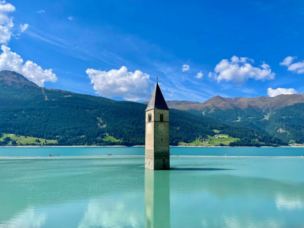 Der Reschensee im Vinschgau ist ein berühmtes Postkartenmotiv - der alte Kirchturm des Ortes schaut noch aus dem Stausee. Bildquelle: © Tommy Krombacher / Unsplash.com